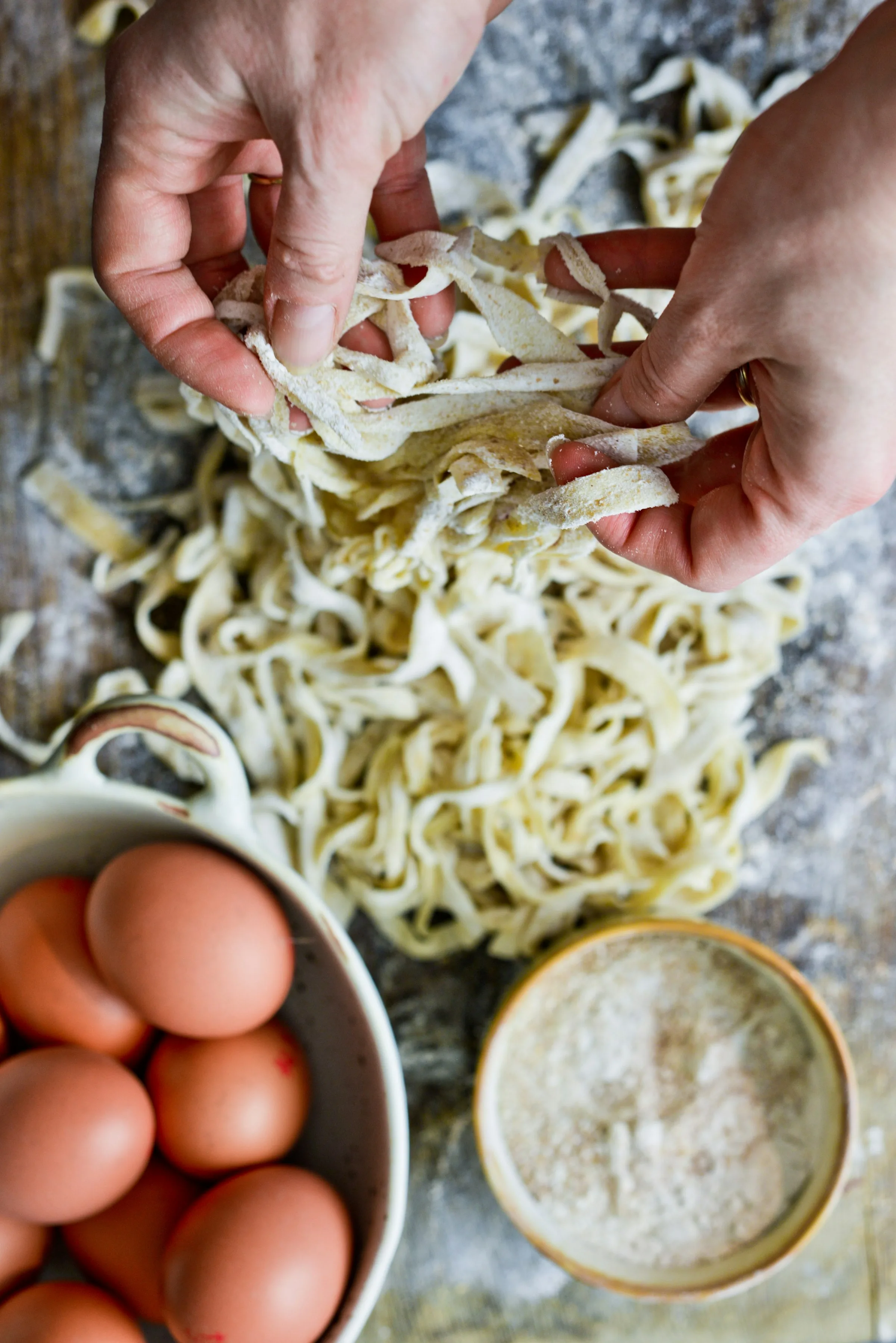 Mani che raccolgono la pasta fresca, accanto a una ciotola di uova