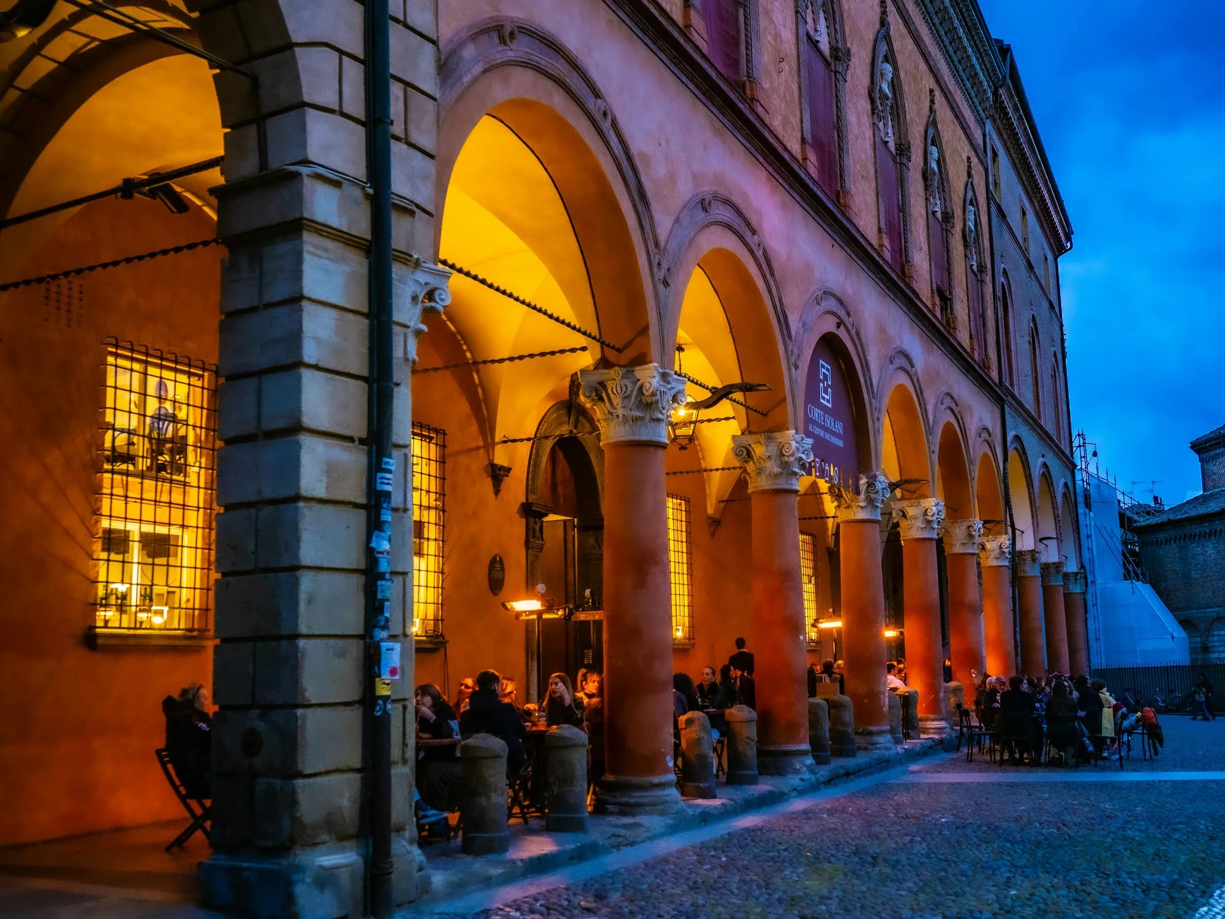 Tavoli apparecchiati sotto le arcate illuminate di un palazzo storico, di sera
