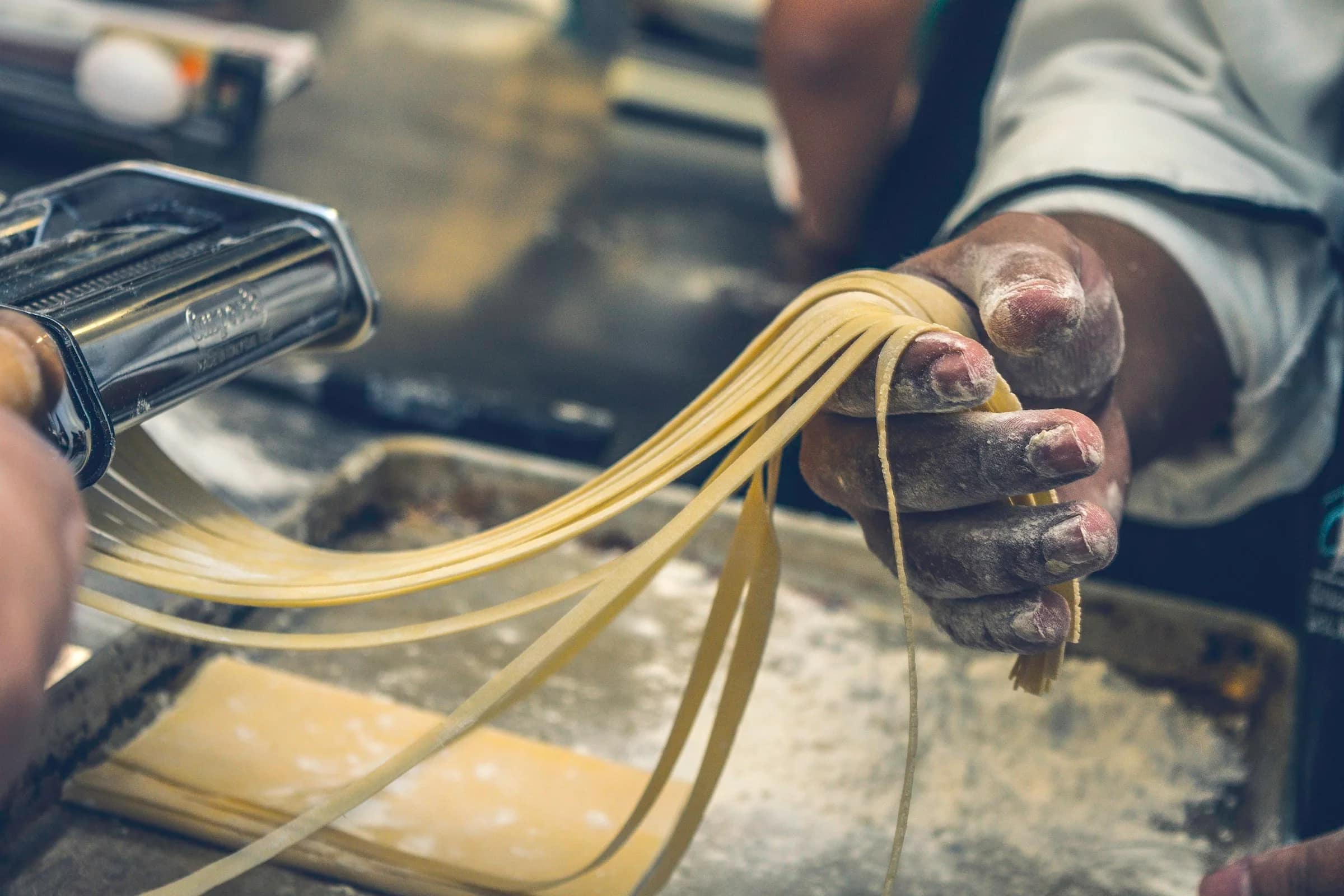 Le mani di una sfoglina sollevano i fili di pasta appena tagliati