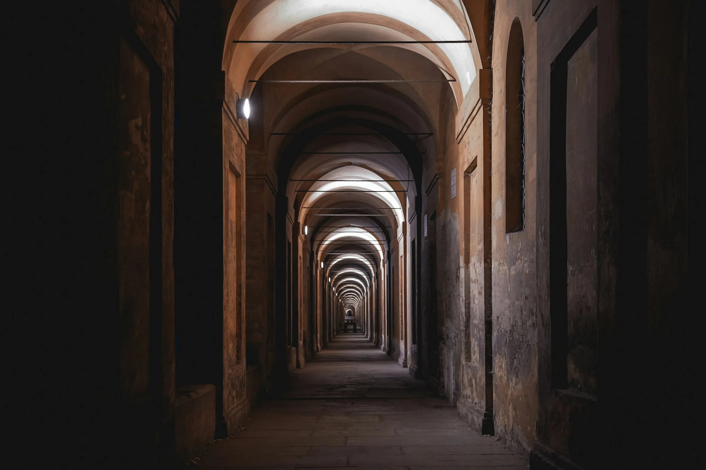 Portico bolognese in penombra, con le volte che si ripetono fino in fondo alla via