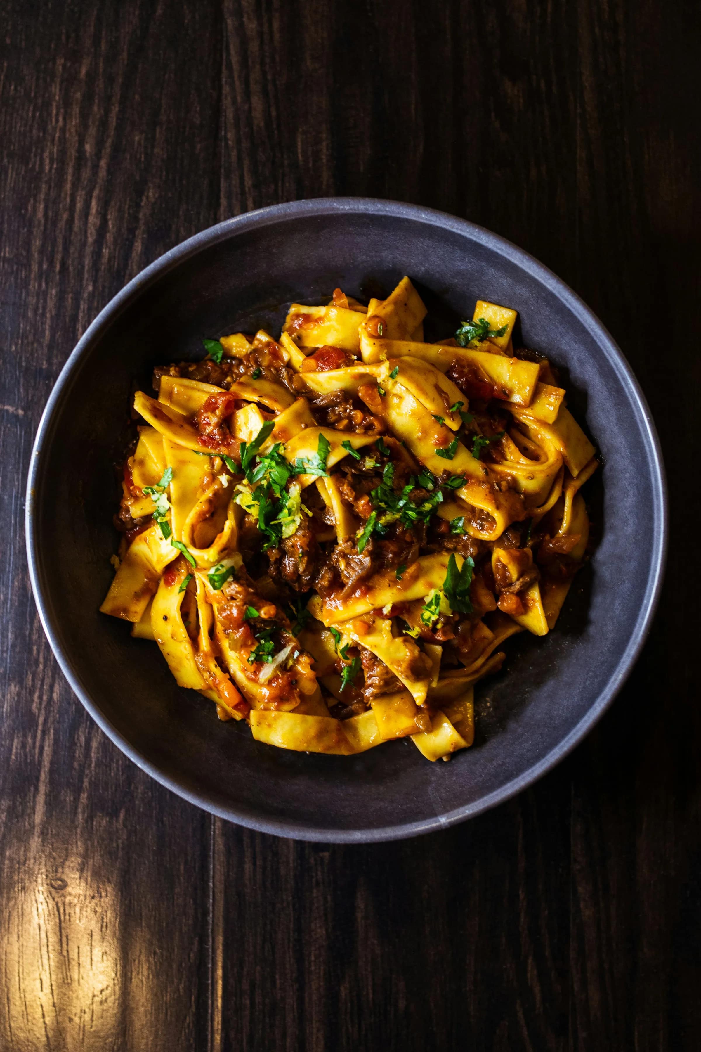 Piatto fondo scuro con tagliatelle al ragù, su un tavolo di legno