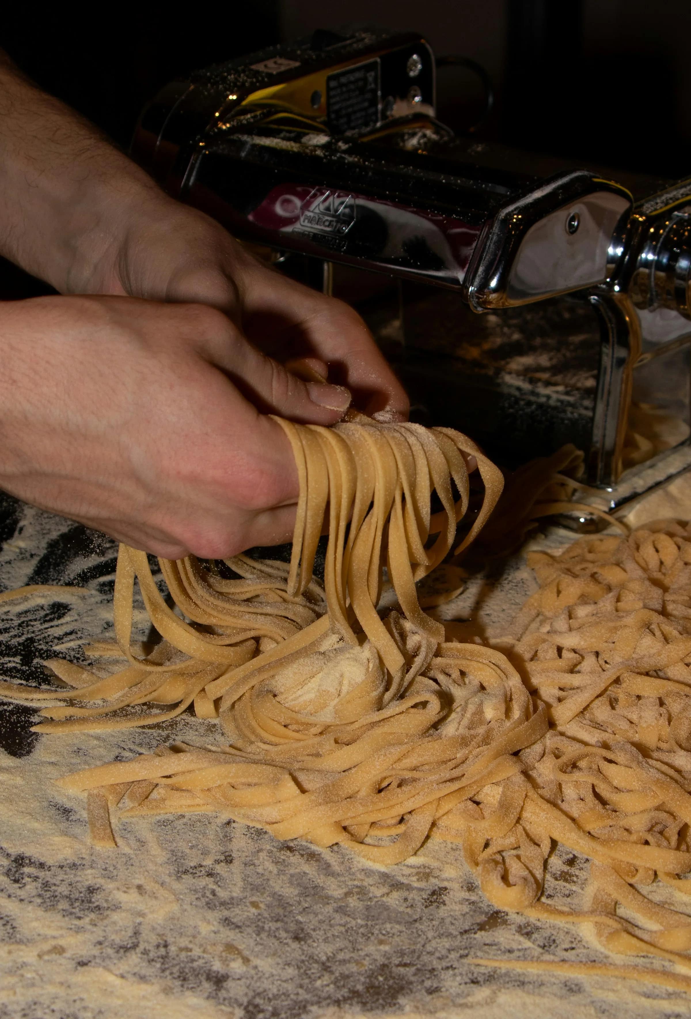 Mani che passano la sfoglia nella macchina per la pasta, in controluce
